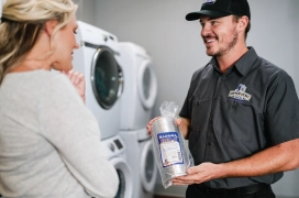 Commercial dryer vent cleaner showing business owner dryer vent hose while standing in front of stacked dryers.